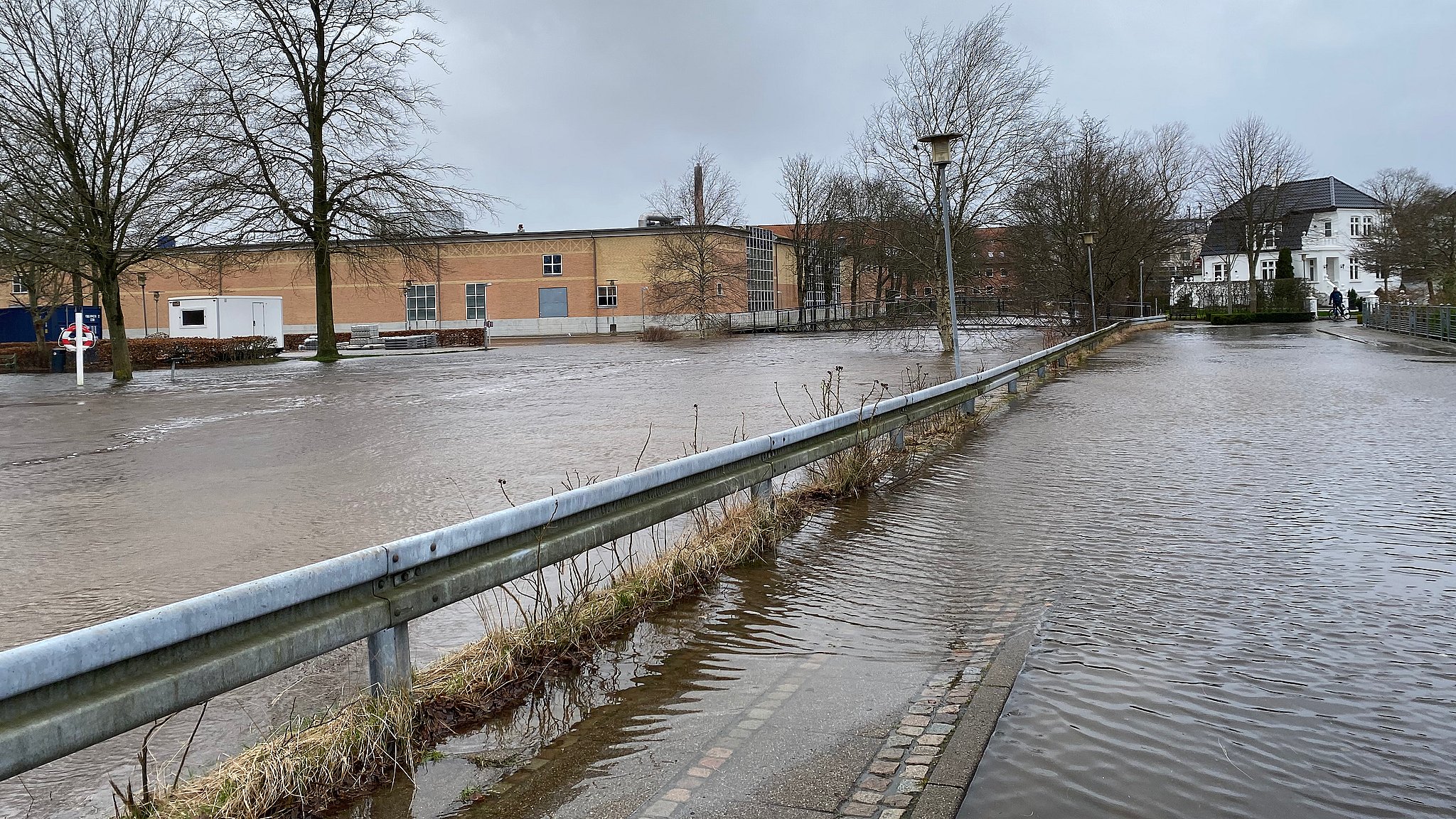 En vej er oversvømmet. I baggrunden ses Kvicklys parkeringsplads.